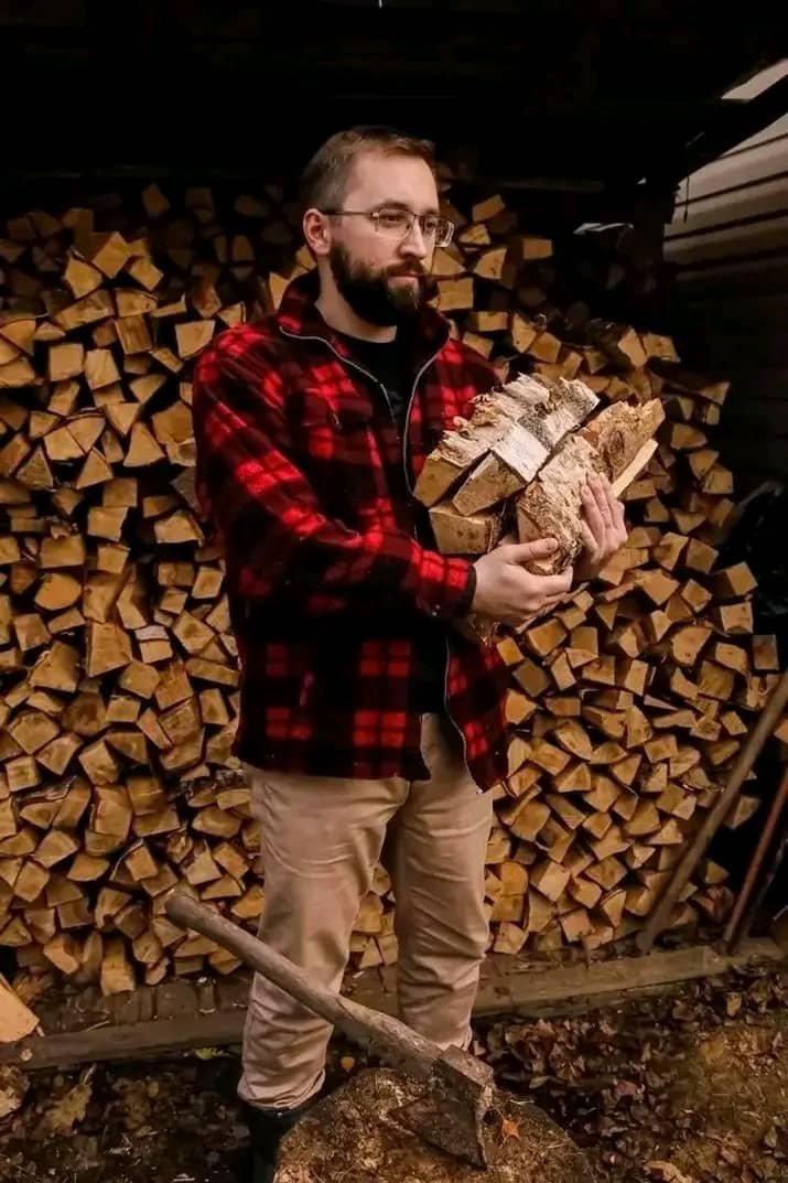 Our founder holding an armful of split firewood in front of the woodpile